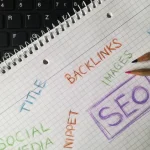 Notebook with SEO terms and pencil beside keyboard